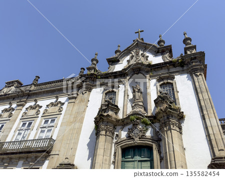 Facade of a historic baroque church with ornate stone carvings, decorative windows, and a central Facade of a historic baroque church with ornate stone carvings, decorative windows, and a central 135582454