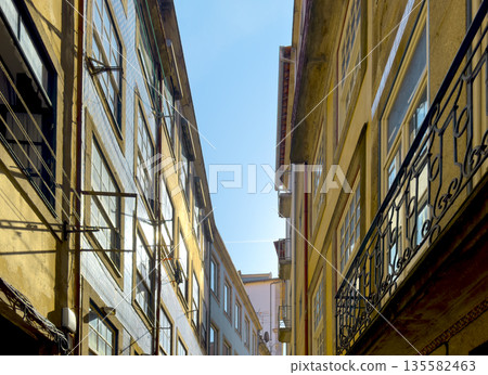 Porto, Portugal, View of narrow street between tall old houses with sunlit facades and wrought iron Porto, Portugal, View of narrow street between tall old houses with sunlit facades and wrought iron 135582463