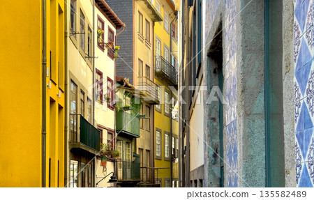 Colorful facades of narrow old houses with green balconies and red window frames. Warm sunlight 135582489