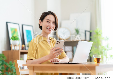 Middle-aged woman looking at a computer in the living room Middle-aged woman looking at a computer in the living room 135582567