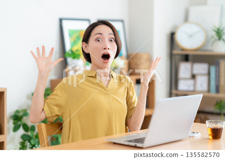 Middle-aged woman looking at a computer in the living room Middle-aged woman looking at a computer in the living room 135582570