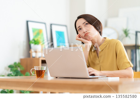 Middle-aged woman looking at a computer in the living room Middle-aged woman looking at a computer in the living room 135582580