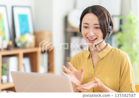 Middle-aged woman looking at a computer in the living room Middle-aged woman looking at a computer in the living room 135582587