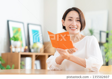 一位中年婦女在客廳看著她的退休金簿。 135582607