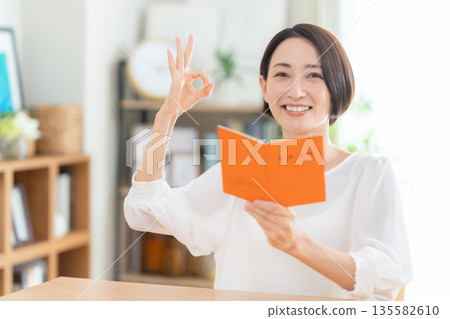 A middle-aged woman looking at her pension book in the living room A middle-aged woman looking at her pension book in the living room 135582610