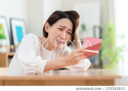 一位中年婦女在客廳查看她的儲蓄存摺。 135582631