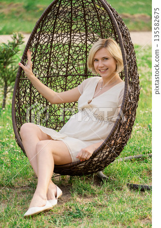 Woman sitting in a hanging chair on a grassy field during daytime Woman sitting in a hanging chair on a grassy field during daytime 135582675
