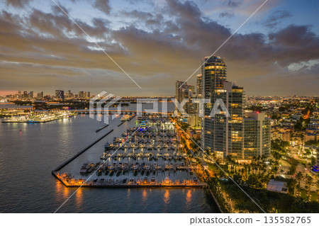 Twilight over Miami skyline and marina. Luxury yachts glowing in the Miami harbor. Sunset cruise near Miami downtown skyscrapers. Aerial night view of Miami Beach at dusk. 135582765