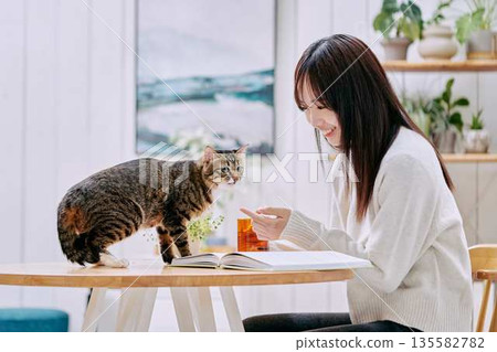 年輕女子在客廳的桌子上和貓咪一起放鬆。 年輕女子在客廳的桌子上和貓咪一起放鬆。 135582782