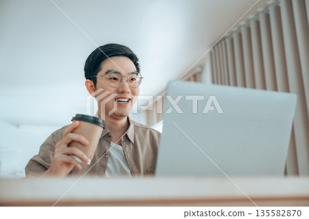 Happy young Asian man working on laptop in living room 135582870