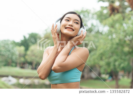 Asian sports woman listening to music on headphones outdoors 135582872