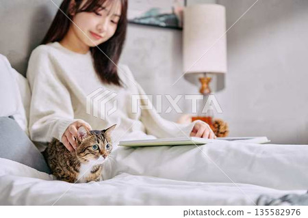 一位女士和她的貓一起在床上放鬆地看書。 一位女士和她的貓一起在床上放鬆地看書。 135582976