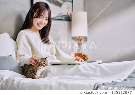 Woman relaxing and reading a book with her cat on the bed Woman relaxing and reading a book with her cat on the bed 135582977