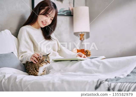 一位女士和她的貓一起在床上放鬆地看書。 一位女士和她的貓一起在床上放鬆地看書。 135582979