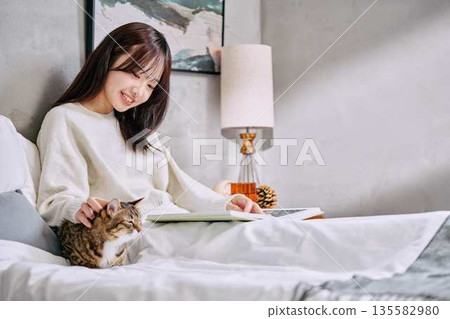Woman relaxing and reading a book with her cat on the bed Woman relaxing and reading a book with her cat on the bed 135582980