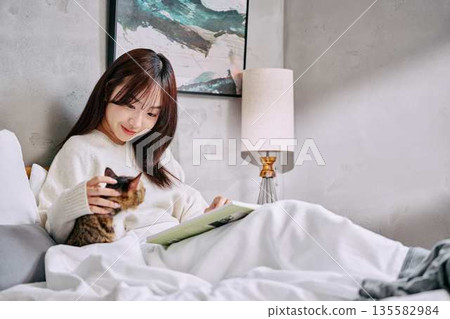 Woman relaxing and reading a book with her cat on the bed 135582984