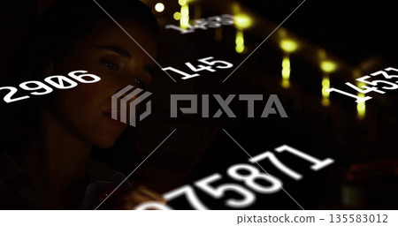 Analyzing woman in button-up shirt interpreting white numeric data in dark control room, copy space 135583012