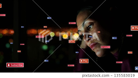 Resting woman wearing dark top by window at night, floating digital icons, city lights, copy space 135583019