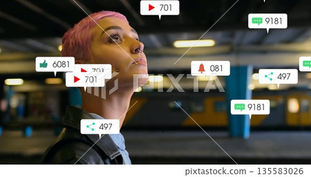 Woman wearing leather jacket with pink hair scanning subway platform, with notification icons Woman wearing leather jacket with pink hair scanning subway platform, with notification icons 135583026