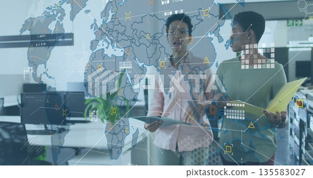 Reviewing digital map overlay two women analyzing data on tablet and folder in open-plan office 135583027