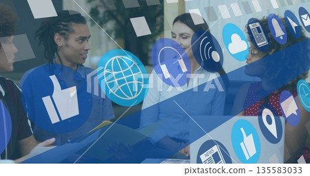 Colleagues collaborating in modern meeting room with tablet, laptop, folder and social media icons 135583033