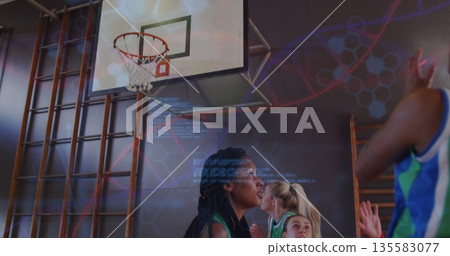 Teammates wearing jerseys positioning for rebound in school gym with basketball hoop and wall bars 135583077