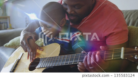 Father and son playing acoustic guitar on sofa in living room, with green throw pillow 135583124
