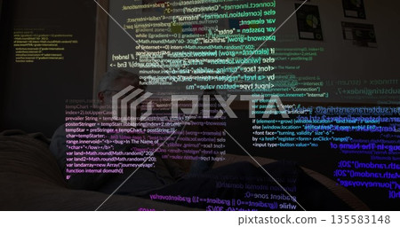Working man typing code on laptop on leather couch in living room, with projected code snippets 135583148