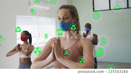 Woman wearing blue mask and beige sportswear holding prayer pose in yoga studio, with green icons 135583168