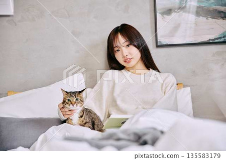一位女士和她的貓一起在床上放鬆地看書。 一位女士和她的貓一起在床上放鬆地看書。 135583179