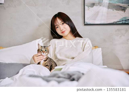 Woman relaxing and reading a book with her cat on the bed Woman relaxing and reading a book with her cat on the bed 135583181