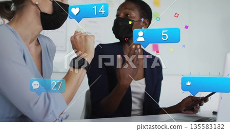 Celebrating women wearing masks exchanging media reactions at meeting table, with laptop and tablet Celebrating women wearing masks exchanging media reactions at meeting table, with laptop and tablet 135583182