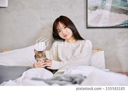 一位女士和她的貓一起在床上放鬆地看書。 135583185