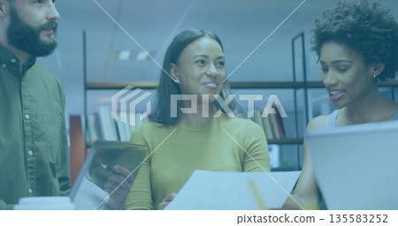 Collaborating colleagues wearing business attire reviewing files in office with laptop tablet books Collaborating colleagues wearing business attire reviewing files in office with laptop tablet books 135583252