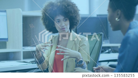 Discussing work, coworker in blazer over red top at office desk, with computers and smartwatch Discussing work, coworker in blazer over red top at office desk, with computers and smartwatch 135583255