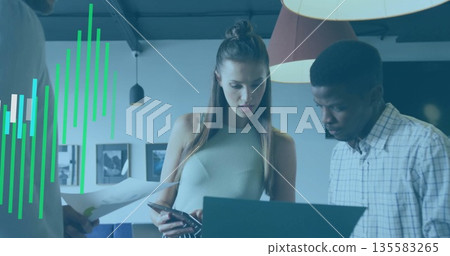 Coworkers assessing charts typing on laptop, consulting smartphone in lounge with pendant lights Coworkers assessing charts typing on laptop, consulting smartphone in lounge with pendant lights 135583265