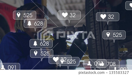 Gloved mechanic in coveralls loosening tire with impact wrench on garage lift, notification icons Gloved mechanic in coveralls loosening tire with impact wrench on garage lift, notification icons 135583327