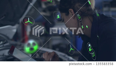 Leaning technician in uniform holding tablet over car hood in garage with AR icons, copy space 135583358