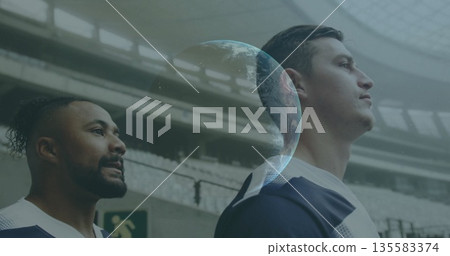 Standing male athletes wearing training jerseys on field in arena, with digital globe hologram 135583374