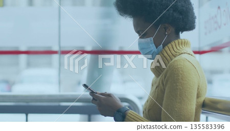Checking smartphone by woman with face mask, yellow sweater in terminal with smartwatch, copy space Checking smartphone by woman with face mask, yellow sweater in terminal with smartwatch, copy space 135583396