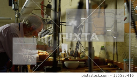 Examining senior craftsman in workshop leaning over workbench under lamp using tools, copy space Examining senior craftsman in workshop leaning over workbench under lamp using tools, copy space 135583416