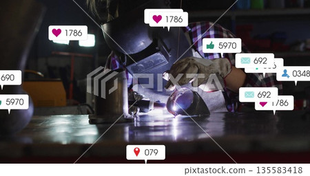 Welding worker wearing helmet gloves shaping pipe with torch at workshop bench showing social icons 135583418