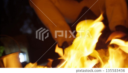 Crackling flames roaring around logs in outdoor fire pit, with boots and pants above Crackling flames roaring around logs in outdoor fire pit, with boots and pants above 135583436