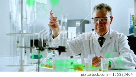 Pipetting chemist wearing lab coat and goggles measuring samples at lab bench, with glassware 135583464