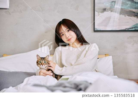 Woman relaxing and reading a book with her cat on the bed Woman relaxing and reading a book with her cat on the bed 135583518
