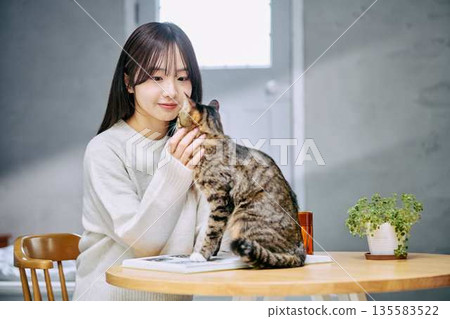 一位女士在桌上撫摸一隻貓。 135583522