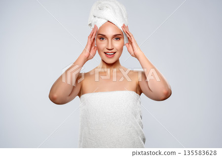 Woman with towel on head smiles while holding her hands on her face in bright setting Woman with towel on head smiles while holding her hands on her face in bright setting 135583628