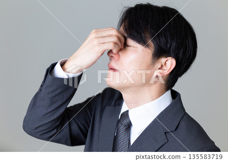 A middle-aged man in a suit suffering and holding his eyes A middle-aged man in a suit suffering and holding his eyes 135583719