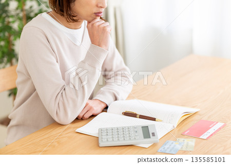 一位中年婦人記帳時憂心忡忡。 一位中年婦人記帳時憂心忡忡。 135585101
