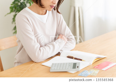 A middle-aged woman worried while keeping a household account book A middle-aged woman worried while keeping a household account book 135585368